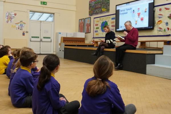 Dysgwyr yn gwrando ar lyfr yn cael ei ddarllen iddynt.